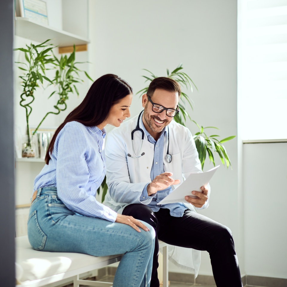 A male doctor and female patient discussing medical results in a bright, comfortable office environment. Modern and friendly setting emphasizing health, trust, and professional care.