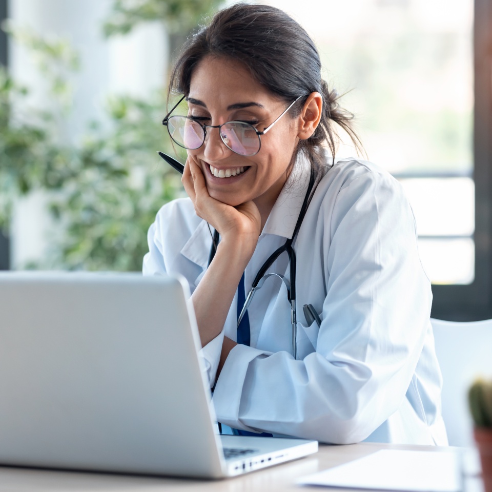 Shot of smiling female doctor working with her laptop in the consultation.