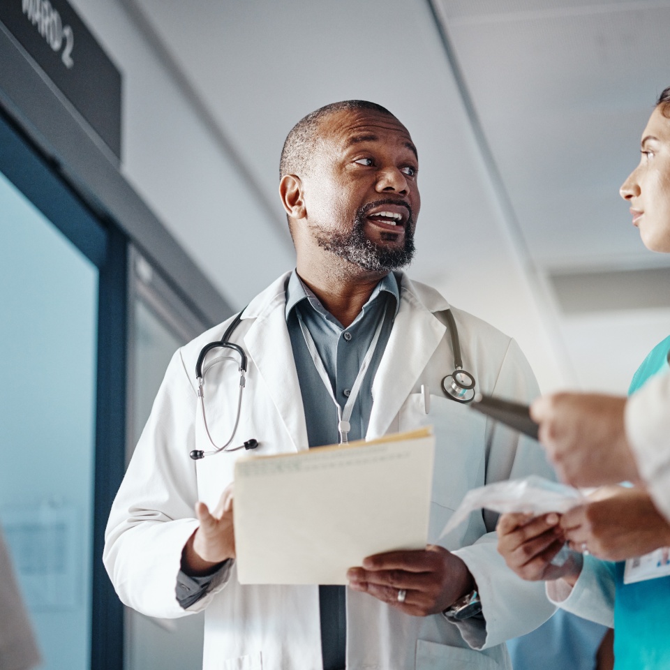 Hospital, teamwork and doctor with folder, conversation and brainstorming for healthcare and administration. Medical, leader and senior professional with group and meeting with documents and clinic.