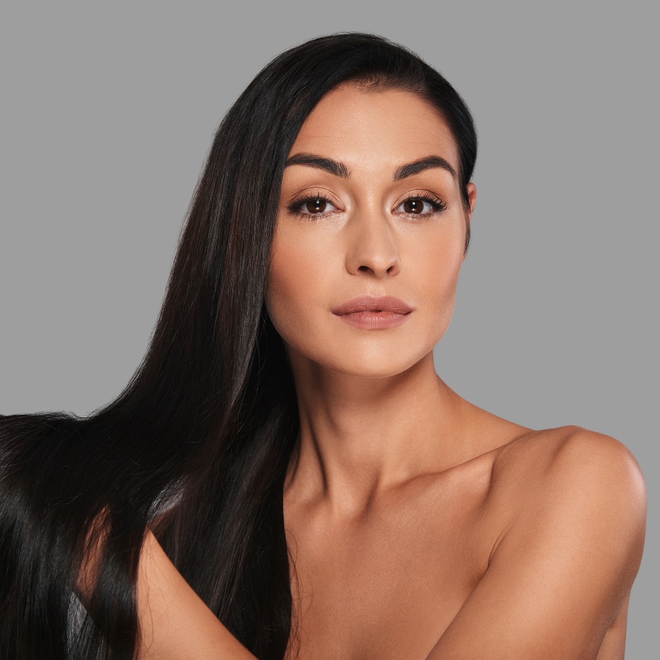 Strong and beautiful hair. Attractive young woman looking at camera with a smile while standing against grey background