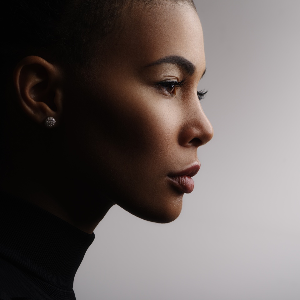 Closeup fashionable portrait of a metis young woman with perfect smooth glowing skin, full lips, collected hair and long neck. Studio photo of an african american female model face, profile