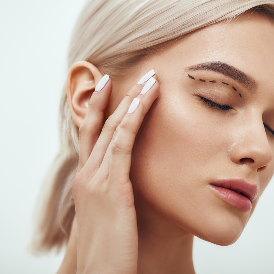 Plastic surgery. Beautiful young blonde woman keeping eyes closed and touching her face with sketch on it