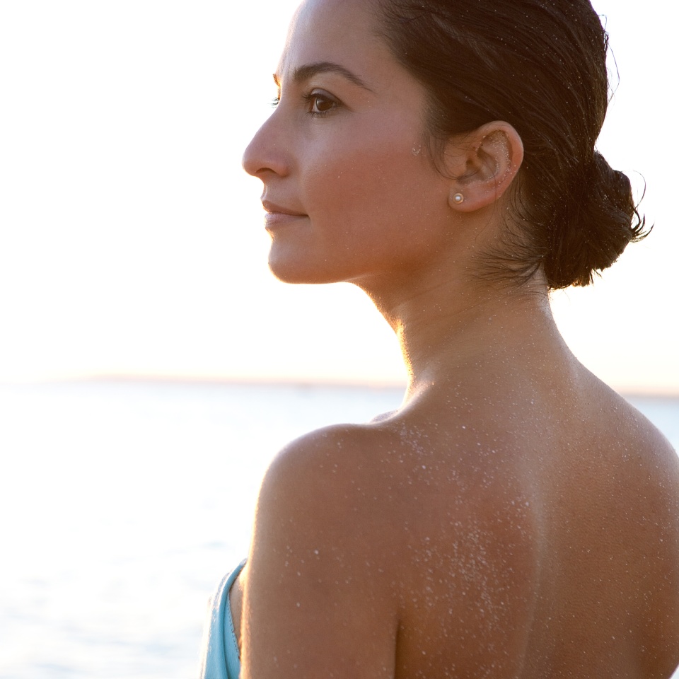 Close up side portrait of a young woman contemplating the scene, standing on a beach and enjoying the blue sea and sky at sunset during a summer vacation.