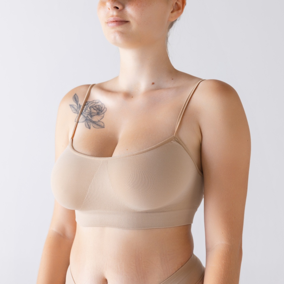 Cropped image of female body, breast in comfortable cotton underwear isolated over grey studio background. Mammoplasty. Concept of beauty, body and skin care, health, plastic surgery, cosmetics, ad