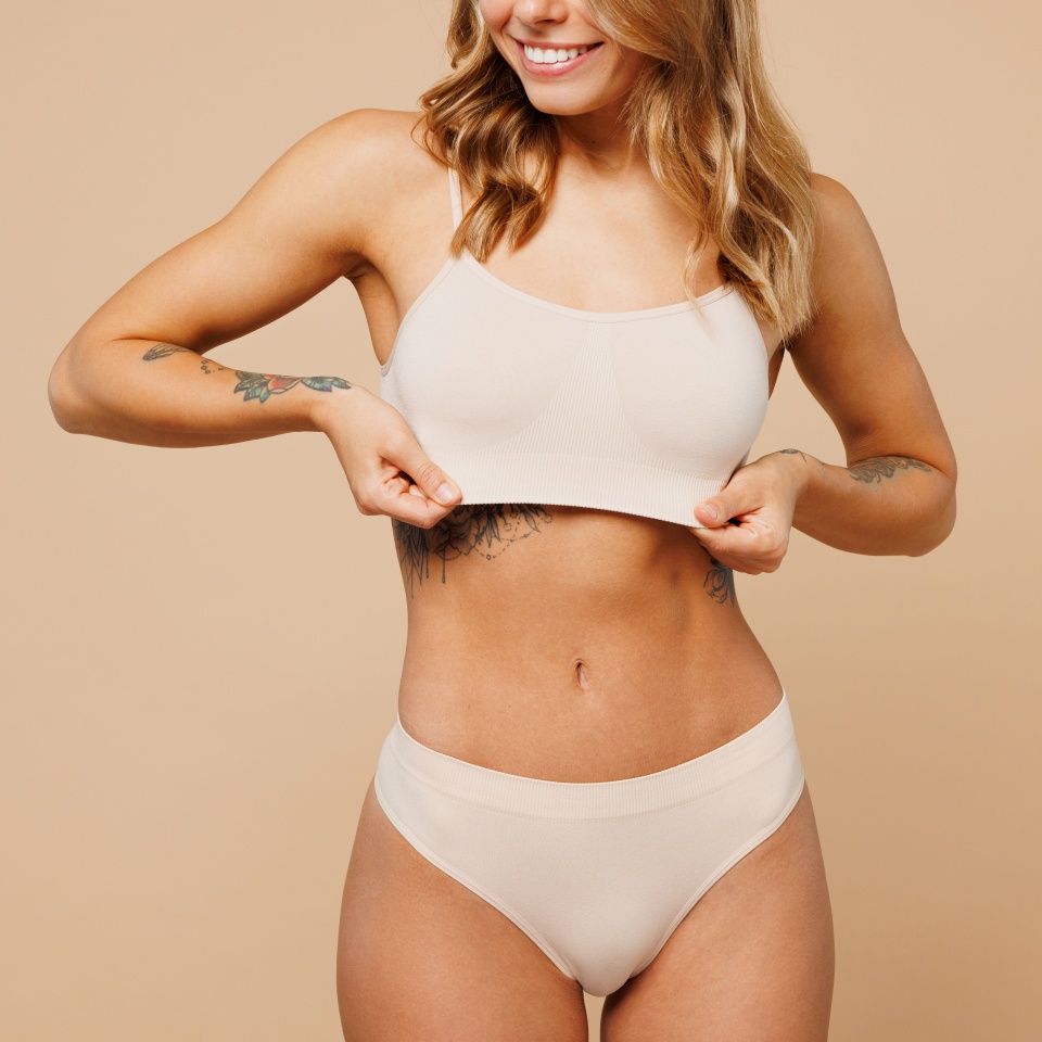 Cropped closed young nice lady woman with slim body perfect skin wear nude lingerie stand hold hands on chest touch top bra isolated on plain pastel light beige background. Lifestyle diet fit concept