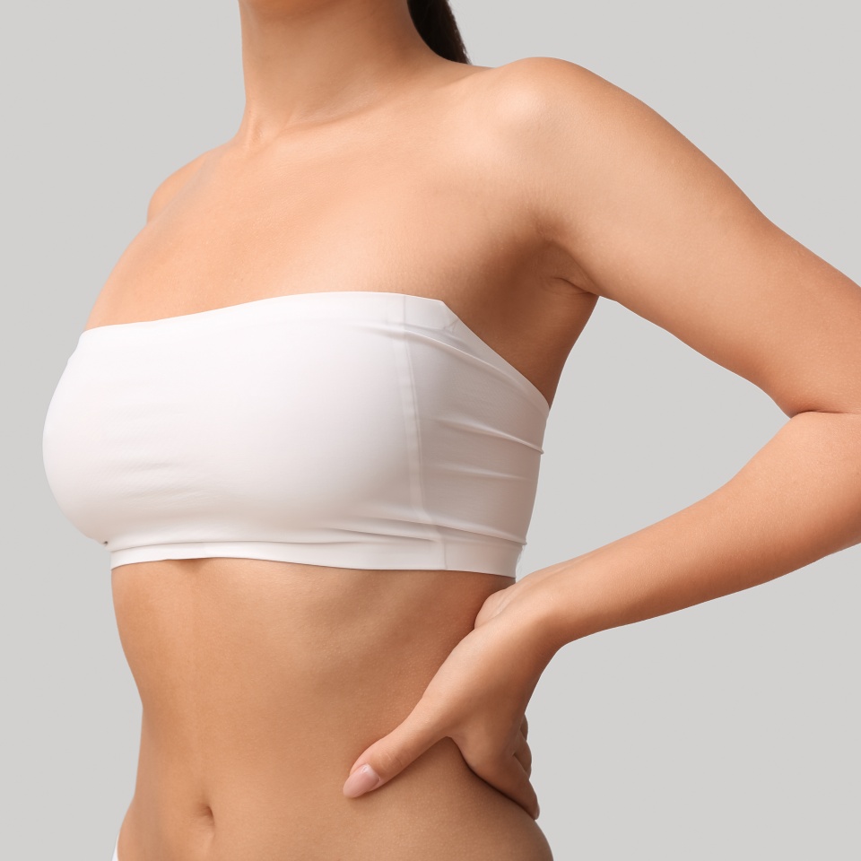 Young woman in bandeau top with beautiful breasts on grey background, closeup