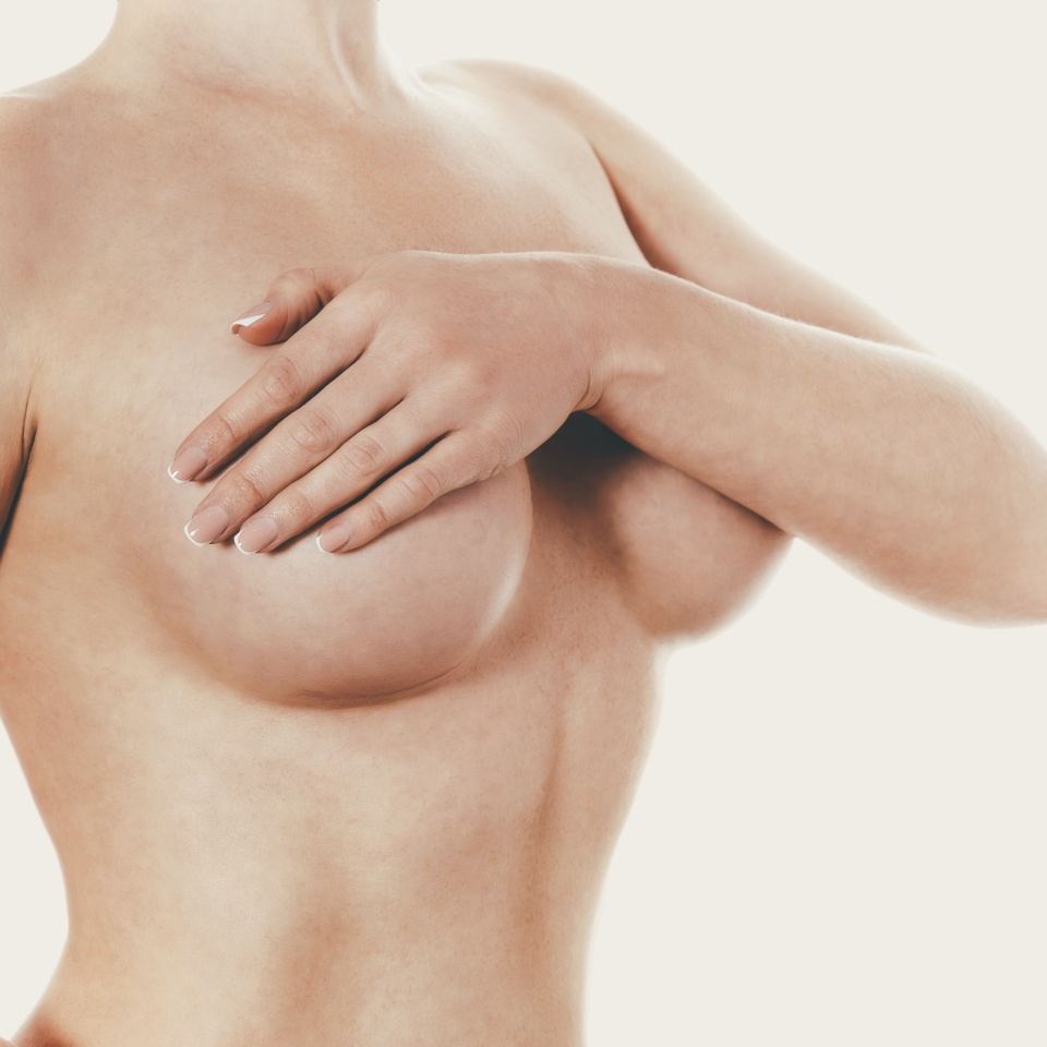 Topless lady on beige background covering breast with hand after breast augmentation. Copy space.