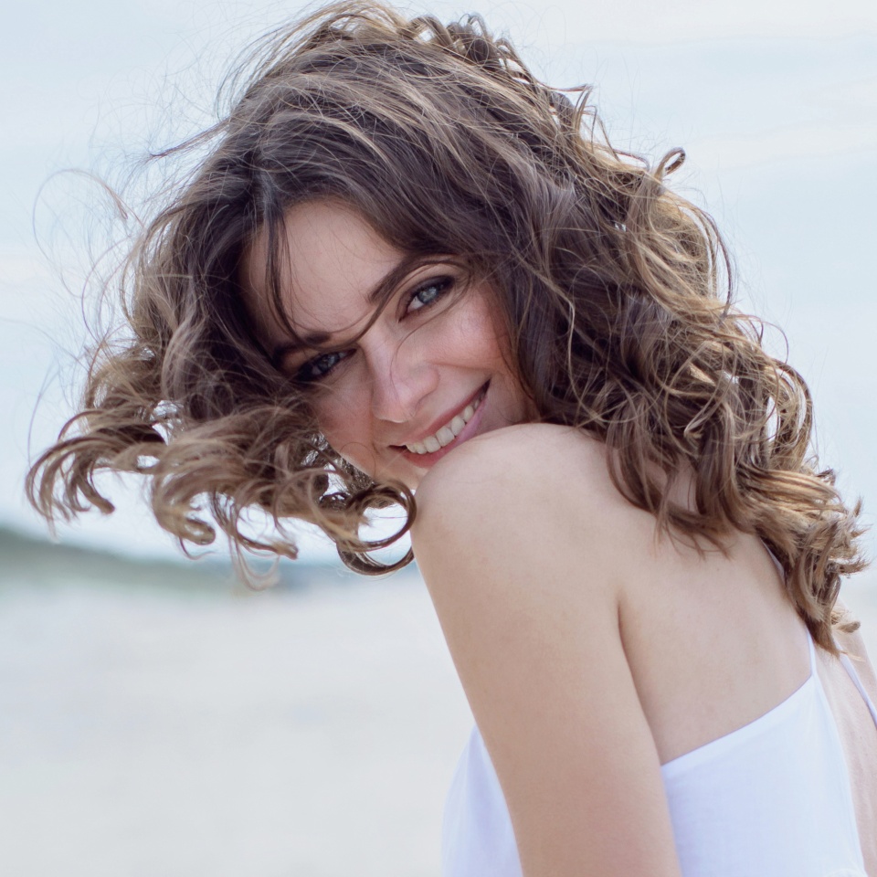 Happy woman on the beach. Portrait of the beautiful girl close-up, the wind fluttering hair. Spring portrait on the beach. Young pretty girl. Young smiling woman outdoors portrait. Close. ocean