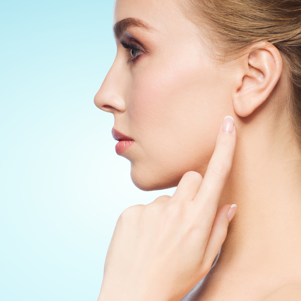health, people and beauty concept - beautiful young woman pointing finger to her ear over blue background