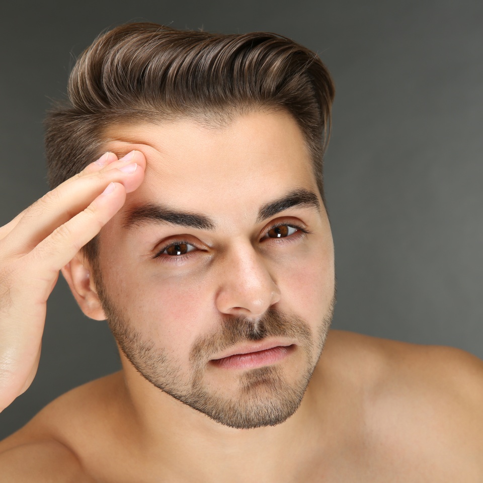 Young handsome man examining his face on grey background