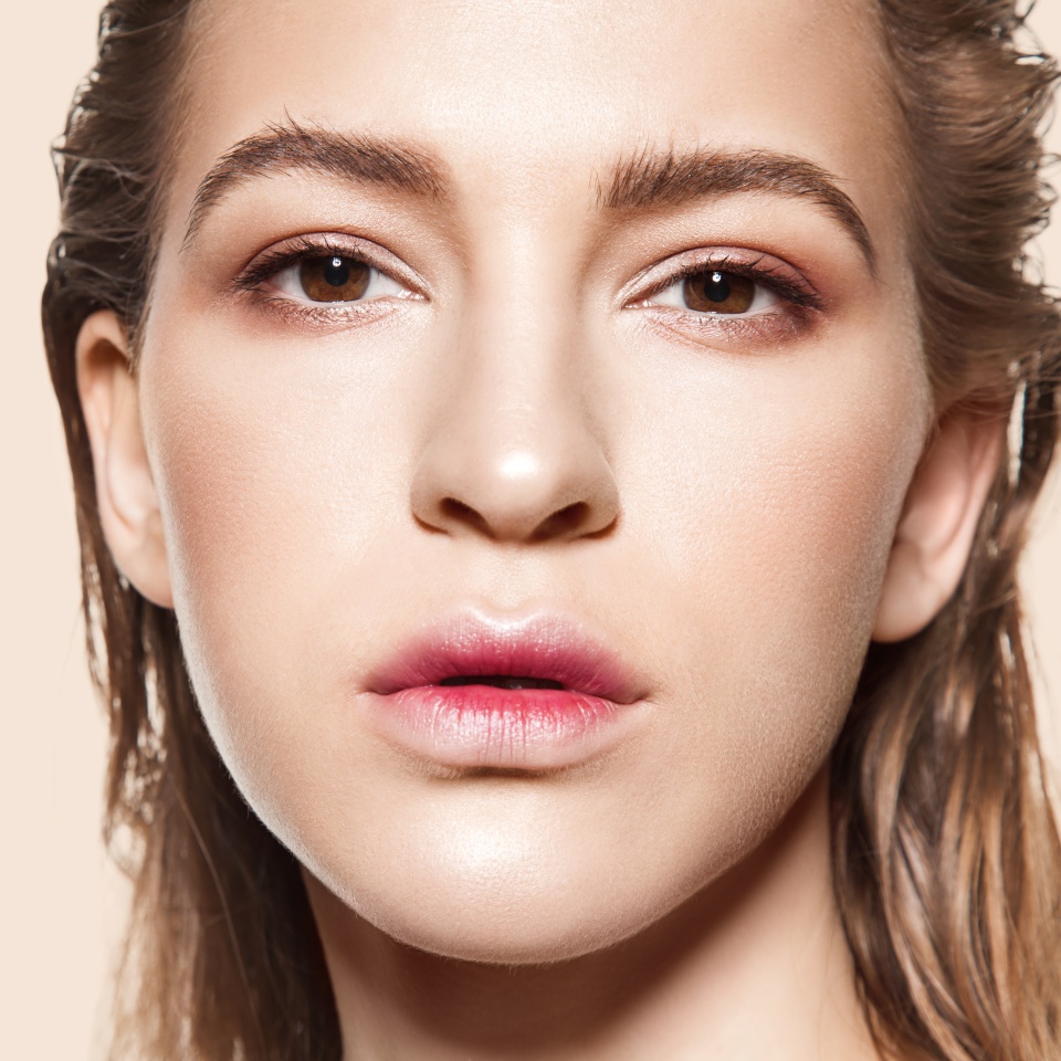Close-up face of fashionable girl with natural make-up and clean beautiful skin looking at camera on beige background