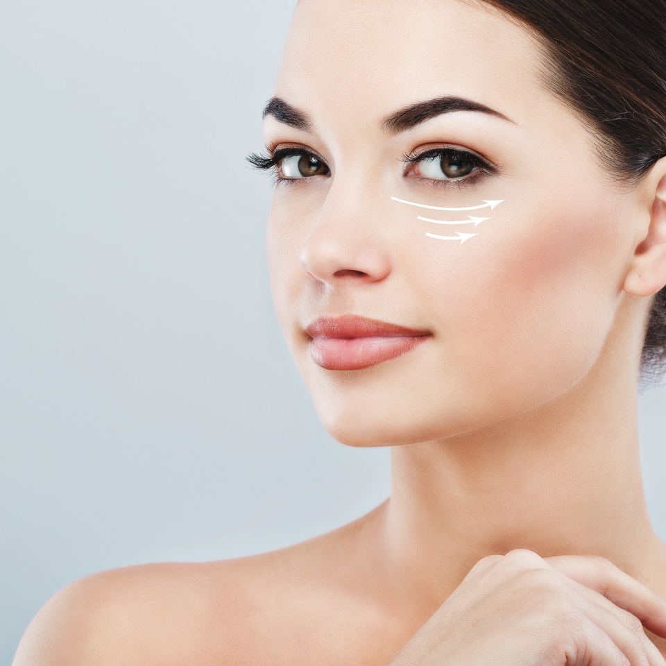 Young female with clean fresh skin, antiaging concept. Attractive girl with naked shoulders, looking at camera and smiling, holding hands near face, lifting arrows under eye